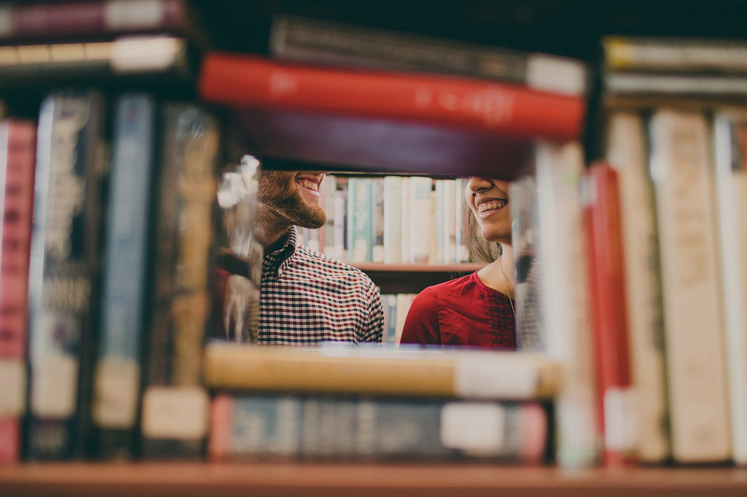 due studenti sorridono attraverso lo scaffale di una biblioteca